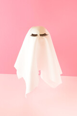 White ghost costume with lashes on a pink background. Romantic Halloween minimal composition.
