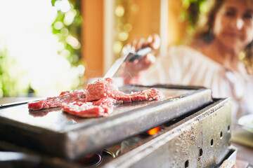 Unrecognizable woman cooking raw meat on stone plate