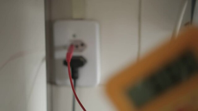 A man checking the voltage in a power Brazilian style outlet socket using a multimer  