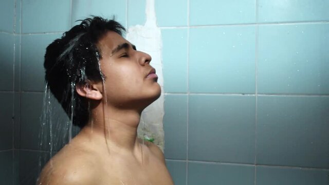 Latin teenager with a lot of black hair, bathing in an aquamarine blue shower, with his eyes closed, concept of toilet, health and personal hygiene, close-up