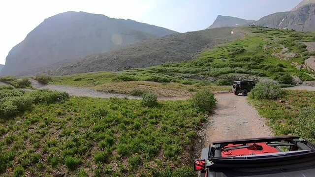Following another 4WD vehicle  on Black Bear Pass trail; passenger wave hands in the air ; spectacular mountain views; concept of adventure, exploration and adrenaline rush