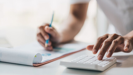 Fototapeta premium Close up of businessman or accountant hand holding pencil working on calculator to calculate financial data report, accountancy document and laptop computer at office, business concept.