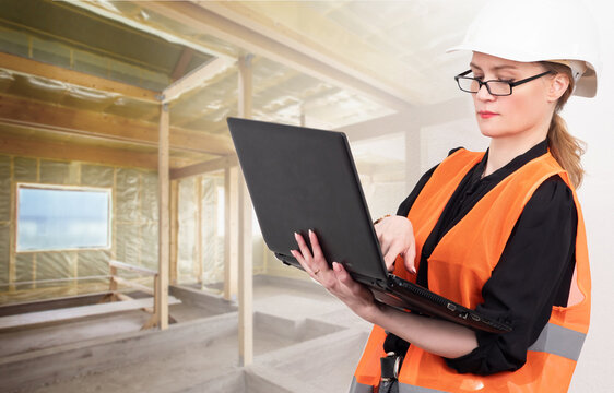 A serious woman works as a civil engineer. A woman with a laptop on a construction site. Engineering control over the construction process. A girl in an orange vest and a white helmet.