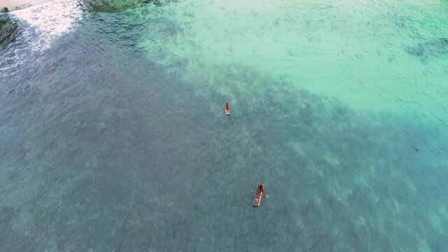 Aerial drone view overlooking people paddling in turquoise waters of the Ilheu das Rolas island
