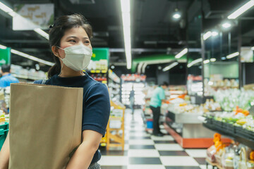 Fototapeta na wymiar young adult asian female woman wearing protective face mask hand choosing fresh product or consumer product in groceries store department mall with care and cheerful new normal shopping lifestyle.