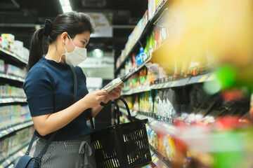 young adult asian female woman wearing protective face mask hand choosing fresh product or consumer product in groceries store department mall with care and cheerful new normal shopping lifestyle. - obrazy, fototapety, plakaty