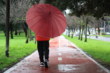 Child with red umbrella, walking on the red path.Winter morning with rain