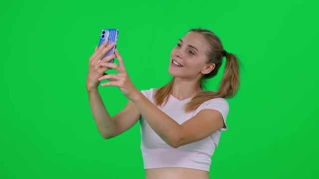 Beautiful caucasian female takes a selfie on a smartphone, young woman takes pictures of herself on a green background, a chroma key template.
