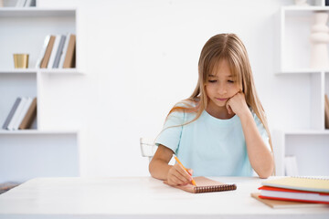 Teenage girl making notes in notepad, doing homework at table at home