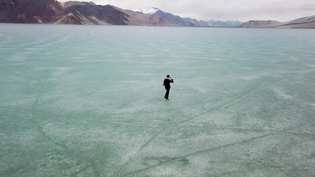 4K on Asian man walking on ice.  Blue Ice surface of Frozen Lake from drone aerial view at Pangong Lake or Pangong Tso, Tso moriri &ndash; Nubra, India. Abstract concept of Cold winter, peaceful and freedom