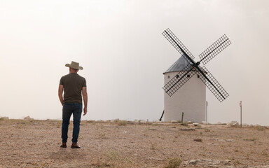 A man wearing a cowboy hat with windmills in the countryside
