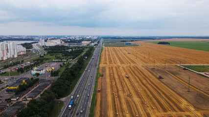 Agricultural machinery on the field. Grain harvesting. Straw bales are lying on the field. There is a busy freeway near the field. Aerial photography.
