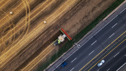 Agricultural machinery on the field. Grain harvesting. Straw bales are lying on the field. There is a busy freeway near the field. Aerial photography.