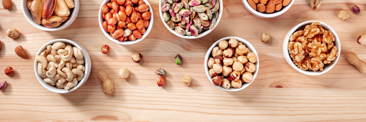 Many different nuts in bowls on a wooden table, healthy vegan snacks panorama
