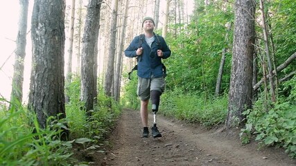 Disabled man with prosthetic limb with backpack walks through forest overcomes path and enjoys. Traveling on foot along forest road and active lifestyle for people with disabilities. active hiking - Powered by Adobe