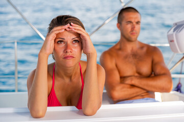 Frustrated woman sitting separately at sailboat during sea cruise, having problems in relationship...