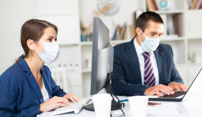 Fototapeta premium Portrait of young business woman focused on work with male colleague in office. People wearing medical face masks to prevent spread of viral infection
