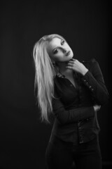 Stylish blond lady with perfect makeup and long straight hair wears blouse, posing at studio. Black and white sho