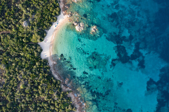 View from above, stunning aerial view of a green coastline with a beautiful beach bathed by a beautiful and turquoise sea. Liscia Ruja, Costa Smeralda, Sardinia, Italy. © Travel Wild
