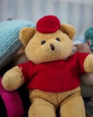The teddy bear is wearing a red shirt. Dolls are toys that are very popular with all ages, from toddlers to the elderly. The shape of the doll also varies. Dolls are generally made of flannel. 