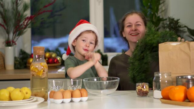 Dancing in kitchen before Christmas. Mom and daughter have fun and cook. Happy family of two sisters. A woman and girl in santa claus hat cook breakfast and dinner. Laugh and eat. Sing songs to music.