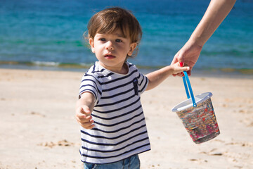 little boy on the beach with bucket held by mother