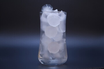 Close-up shot, showing the ice in clear glass of water melting on black background as the temperature rises. Media about global warming from world climate change and the greenhouse effect.