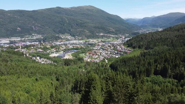 Panoramic view over F&oslash;rde city from a distance - Rotating aerial behind lush forest with parallax effect - Norway