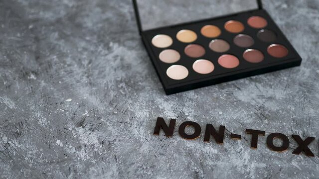 low tox and natural beauty products, make-up palette with non-toxic text on grey background