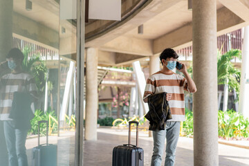 Travel. A man wearing glasses with a striped shirt and mask is talking on a mobile phone. carries jacket on the right hand and luggage is placed on the right