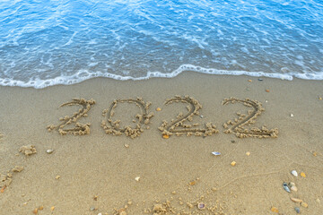 The numbers 2022 are written in the sand. New year on the beach. Sea coast, wave. Place for your text. Summer in winter. Vacation on the ocean. Copy space.