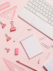 Girly office and school equipment. Pink ruler, paper clips, empty notebook, pens, and laptop isolated on a pastel pink background. Creative office or school concept with copy space. Flat lay.