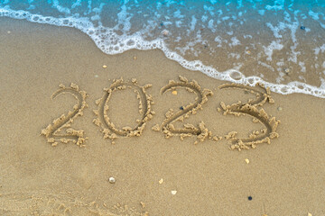 Fototapeta na wymiar The numbers 2023 are written on a sandy seashell beach. Wave and surf. Summer New Year. Vacation, resort and recreation. Nature. Sea coast