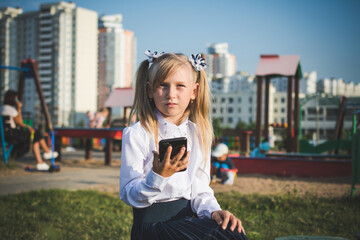 Fototapeta premium Little girl on the street talking on the phone and writing a message on the playground