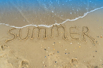The word summer is written on the yellow sand of the beach. Blue wave and surf. Resort and vacation. Summer on the seaside. Relaxation rest concept