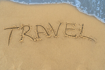 Travel concept - inscription in the sand. Sandy coast of the sea. Motivation. Ocean wave. The word travel is written on the sea beach. Vacations on the shore