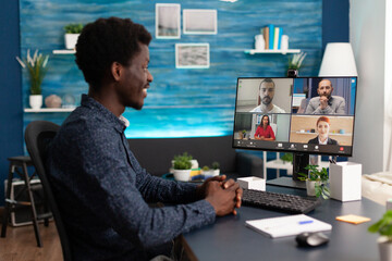 Obraz na płótnie Canvas Man of african ethnicity using conference webcam communication to connect via internet with coworkers while working from home. Black person remote worker chatting about job duties