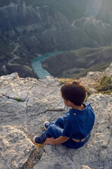 boy child in a blue linen jumpsuit sit on the cliff of the Sulak canyon in Dagestan and thinks about life