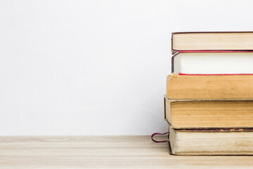 stack of old books on a wooden table with a white wall.
