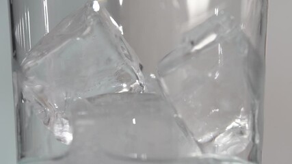 Macro Ice cubes in clear tall class have clear liquid poured in slow motion 4k