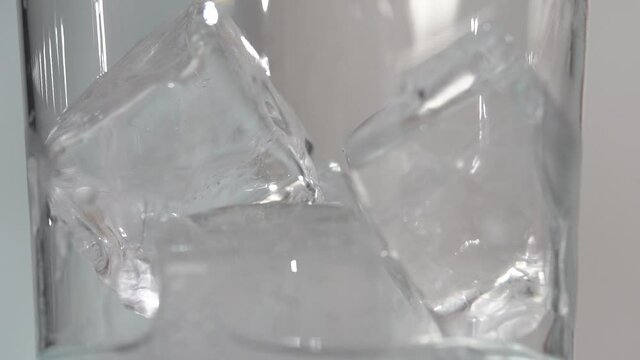 Macro Ice cubes in clear tall class have clear liquid poured in slow motion 4k