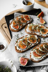Fototapeta na wymiar toast with figs, cream cheese and thyme on a black plate, ingredients on the breakfast table, healthy vegetarian snack or dish, white background, close up, flat lay