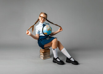 schoolgirl isolated on yellow background with globe. little girl in school uniform sitting on a...