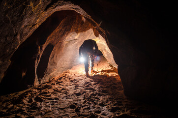 A man with a flashlight goes to the sandstone cave. - obrazy, fototapety, plakaty