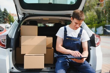 Young male courier with parcels near delivery service car