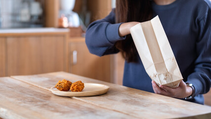 Closeup image of a young woman picking fried chicken from paper food bag and putting in a plate at home for food delivery concept