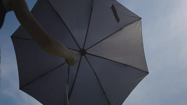 The girl lays out an umbrella against the blue sky.