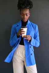 Young african woman with a blue jacket suit and a coffee over black background.