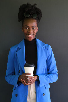 Smiling African Woman With Blue Jacket Suit And A Coffee Over Black Background.