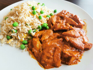 Indian chicken curry with egg fried rice with green peas on a plate.  
